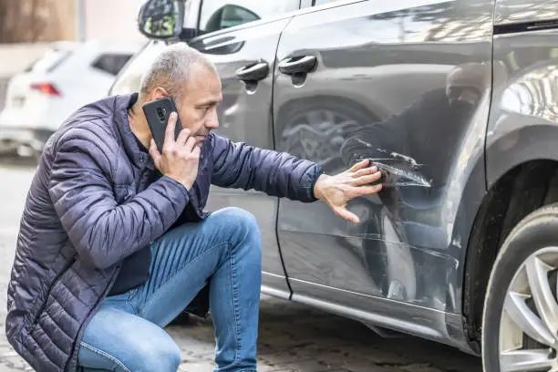 Șofer care sună la centrul de daune de lângă mașina lovită